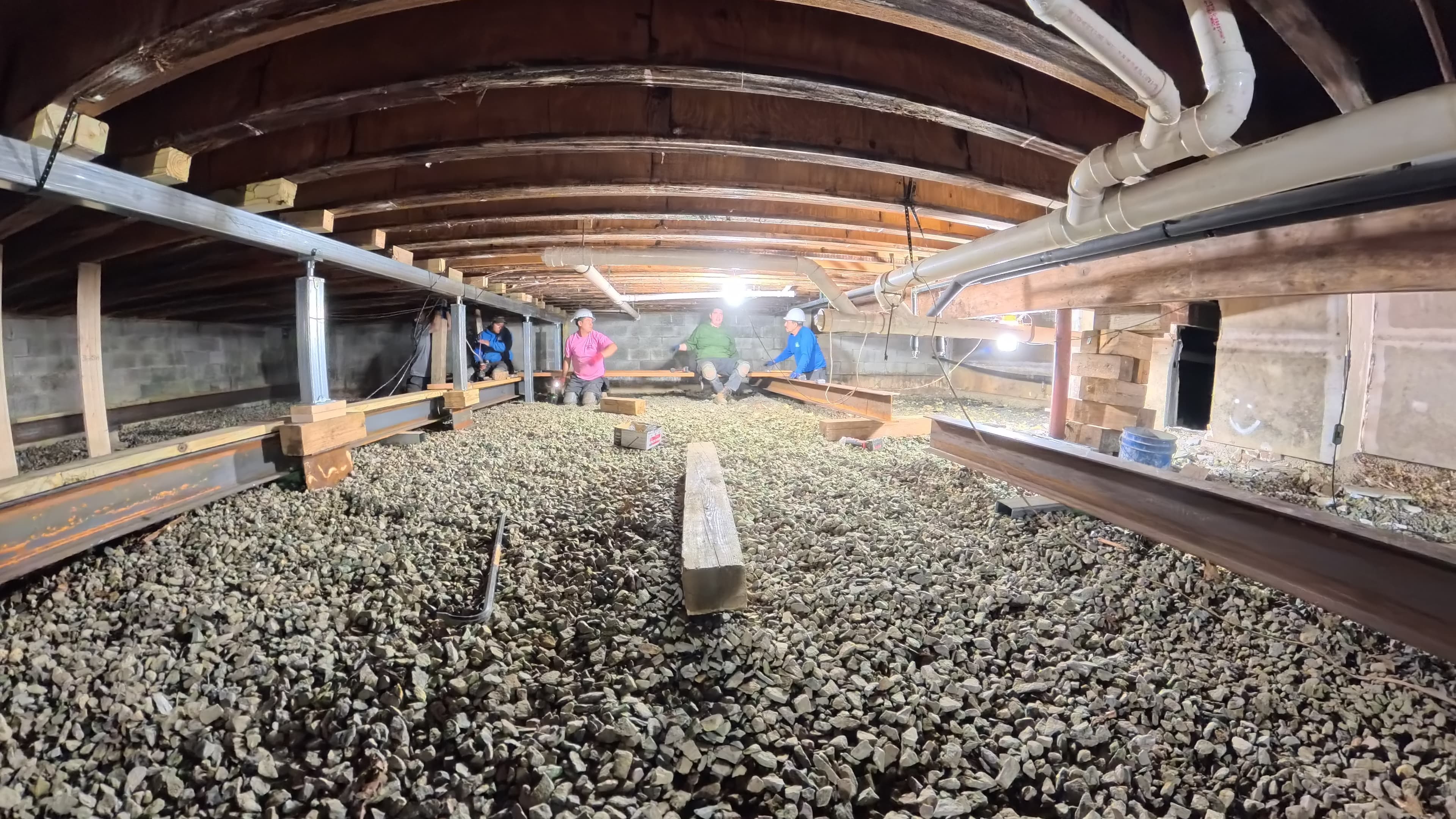 Crew positioning steel I-beams in the confined crawl space of the infirmary in Barryville, NY